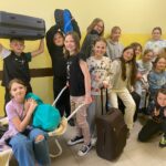 Fotografia przedstawia uczniów klasy czwartek trzymających walizki, taczkę, koszyki zamiast plecaków.