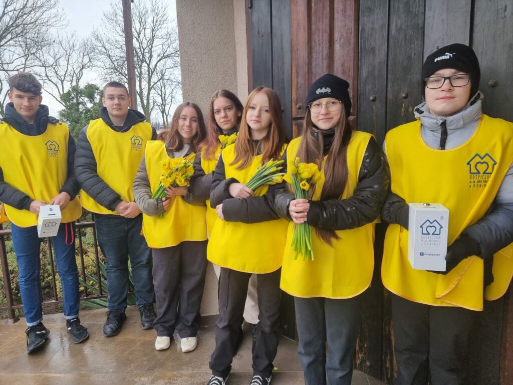 Uczniowie naszej szkoły stoją pod kościołem w żółtych kamizelkach trzymają żonkile symbol nadziei.