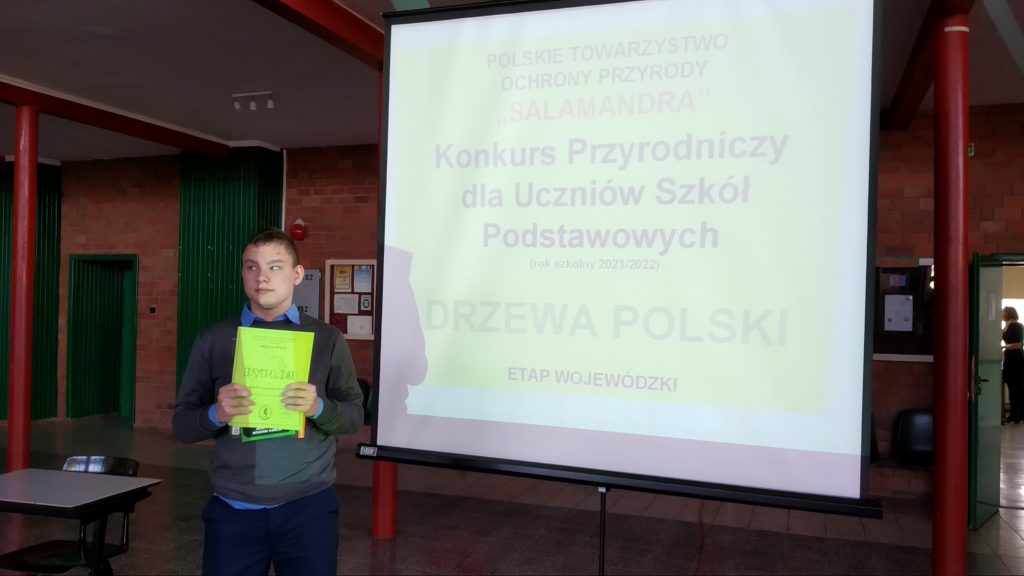 Fotografia przestawia Jakuba stojącego z dyplomem potwierdzającym udział w konkursie.