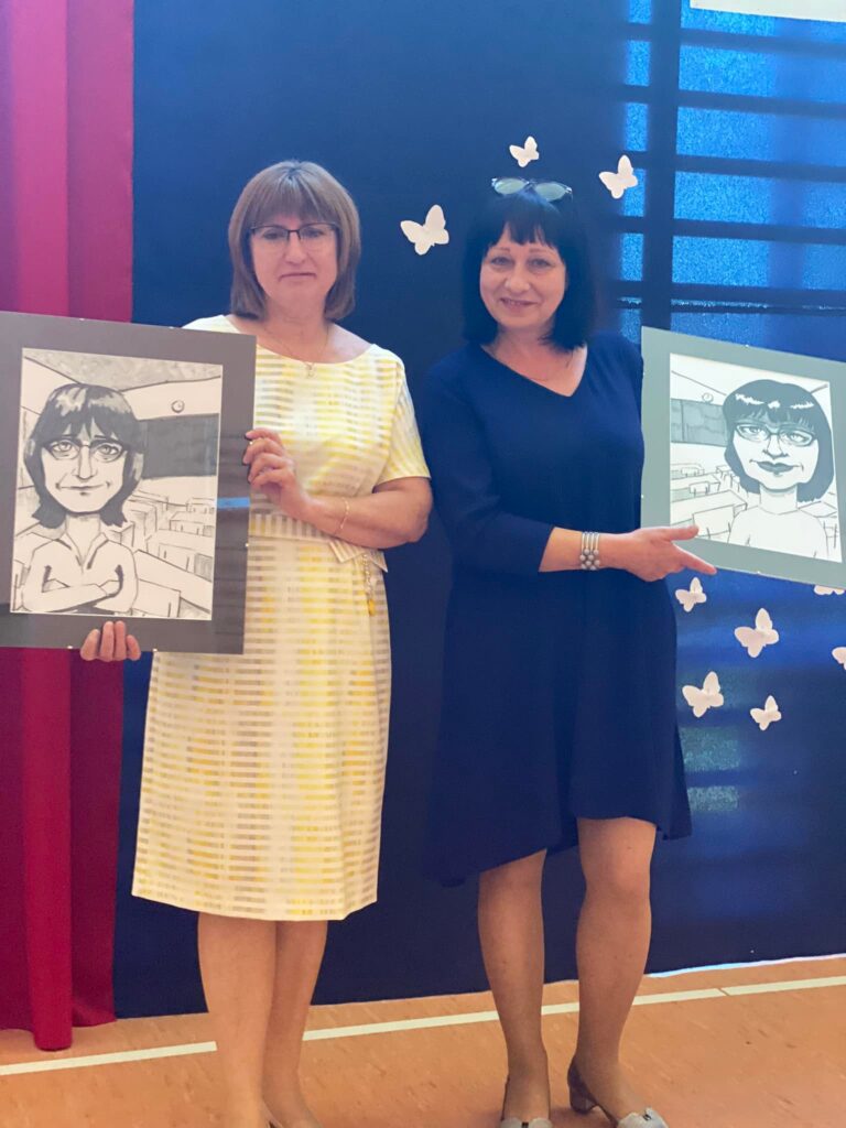 Fotografia przedstawia panią Wiolettę Rzepecką i Krystynę Okulską trzymające obrazy przedstawiające ich karykatury.