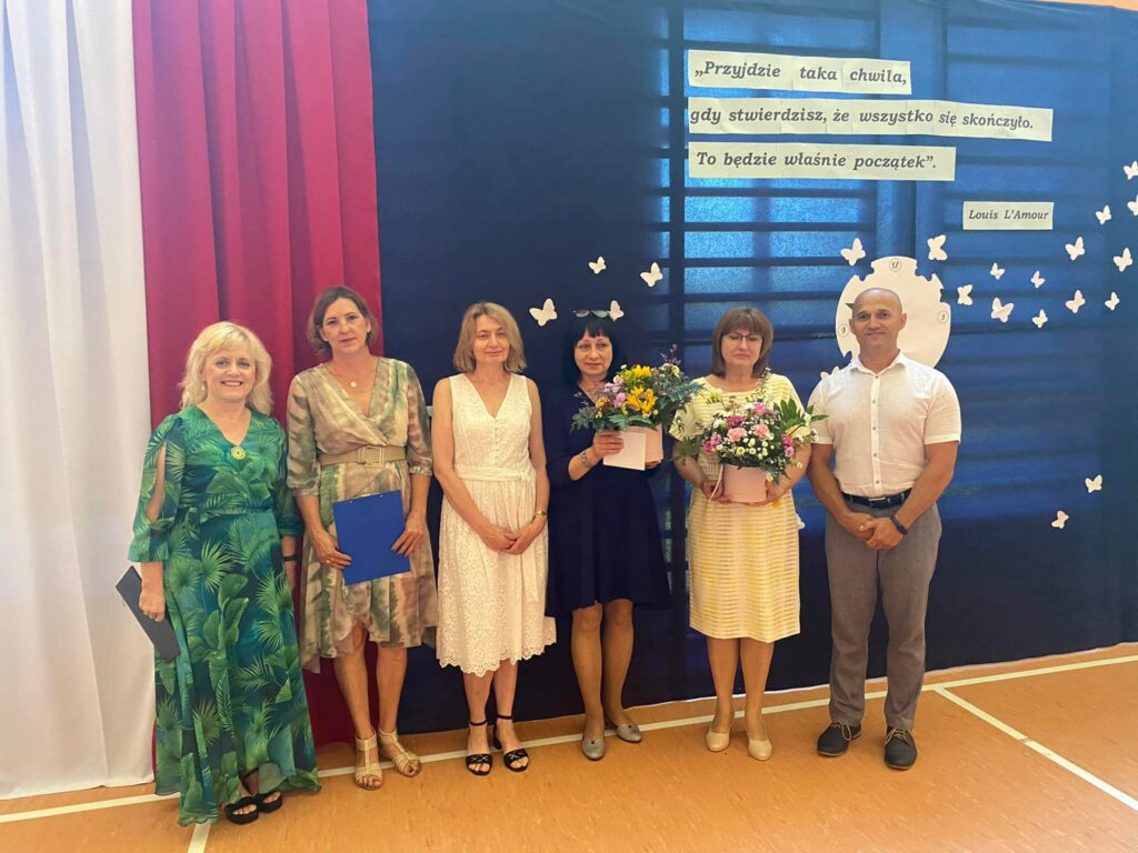 Fotografia przedstawia panie odchodzące na emeryturę trzymające kwiaty. Po boku stoją: pani dyrektor, pracownik szkoły oraz nauczyciel.  