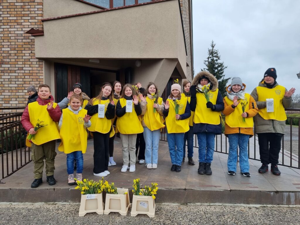 Uczniowie naszej szkoły stoją pod kościołem w żółtych kamizelkach.