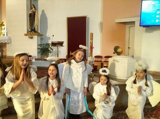 Zdjęcia przedstawiają uczniów, którzy grają w Jasełkach. Chłopcy przebrani są za pasterzy, dziewczynki za aniołów. Na krzesłach przy stajence siedzi Maryja i Józef.