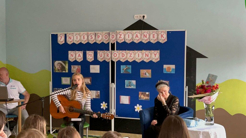 Fotografia przestawia poetkę Danutę Olczak praz uczennicę Ninę Gajewską grająca na gitarze i śpiewającą.