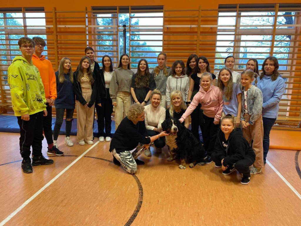 grupa uczniów i nauczycieli w sali gimnastycznej z psem rasy berneński pies pastewny