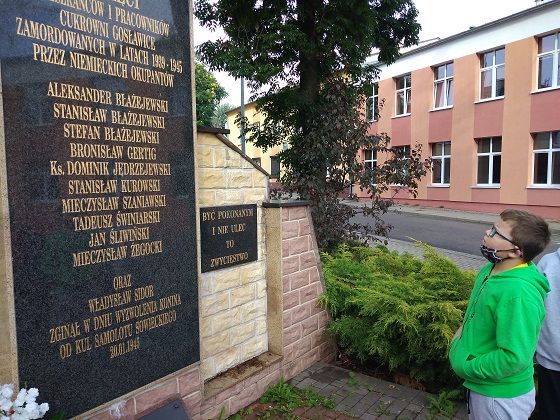 Fotografia przedstawia ucznia stojącego przy pomniku poległych pracowników i mieszkańców Cukrowni Gosławice.