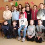 Obrazek przedstawia grupę dzieci, ubranych na czerwoną, śpiewających polskie kolędy