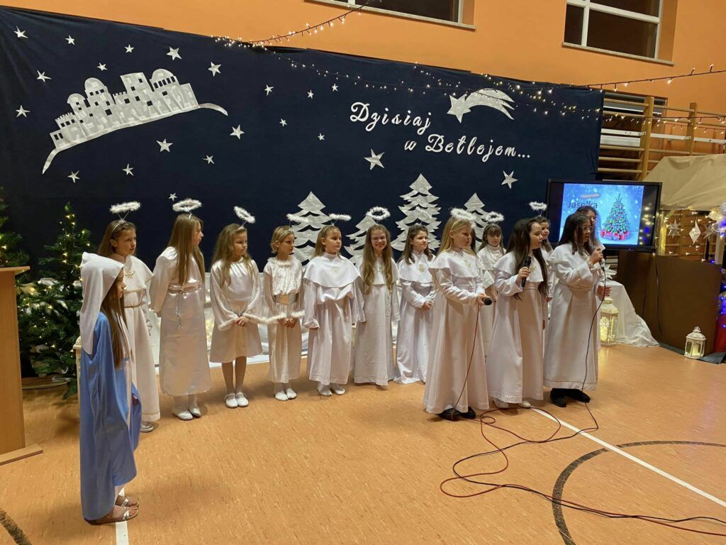Dziewczynki na tle napisu dzisiaj w Betlejem stoją w białych sukniach i śpiewają kolędę