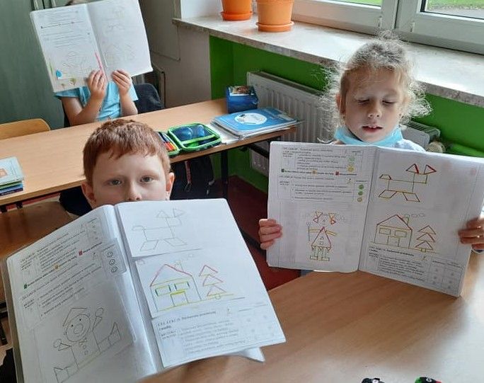 Fotografia przedstawia uczniów klasy pierwszej trzymających swoje otwarte zeszyty. 